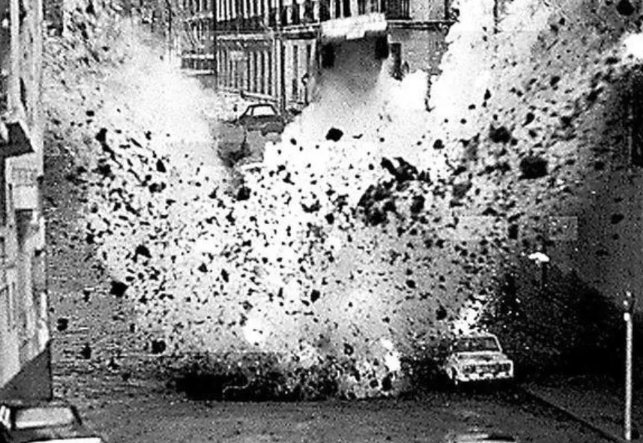 Eine s/w Aufnahme einer nachgestellten Filmszene in der eine Bombe mit enormer Splitterwirkung explodiert und ein Auto viele Meter hochschleudert.