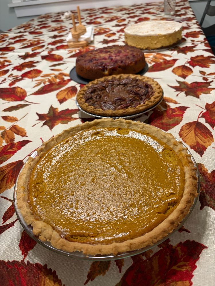 An array of desserts with pumpkin pie in the forefront, then pecan, cranberry upside down cake, and pumpkin cheesecake 