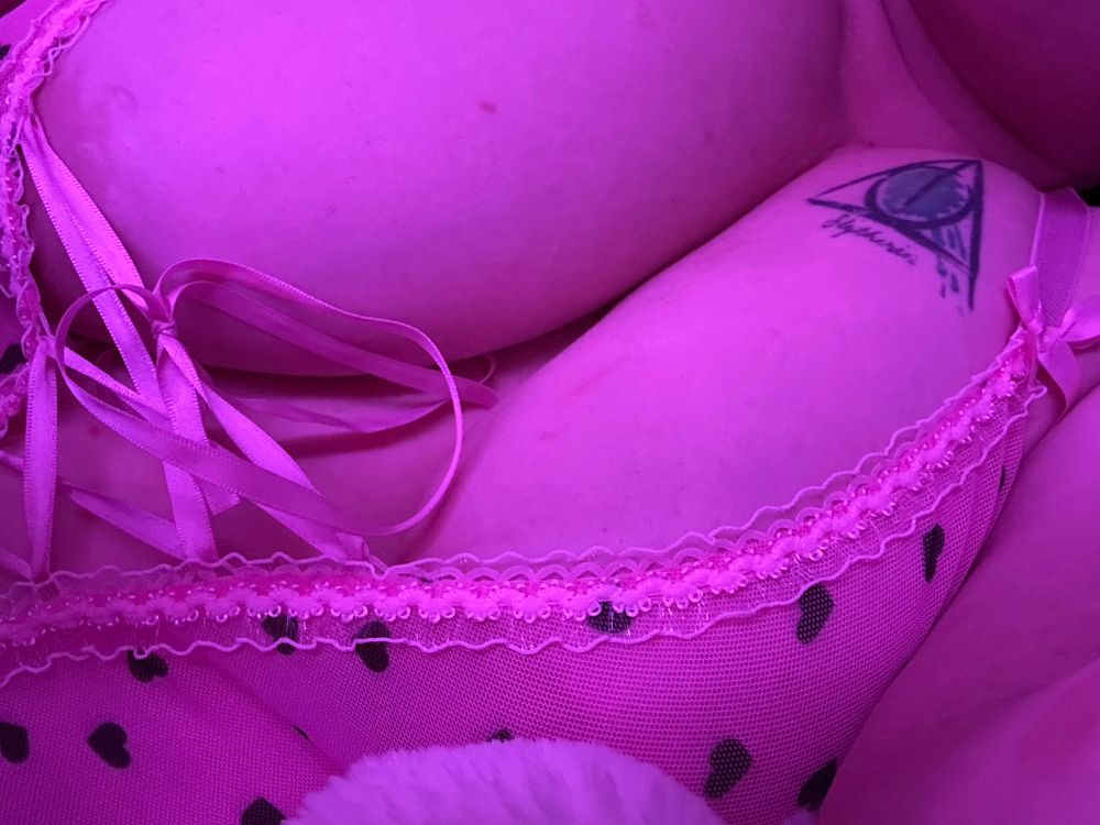 You have an extreme closeup view of Lorelai’s cleavage as she lounges on her side in a light pink bodysuit covered in small black hearts. The pink ribbon laced up the center strains against her large breasts, just barely preventing them from spilling out as you get a glimpse of her nipples through the semi-sheer fabric. 