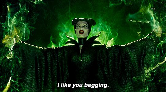 Live action maleficent, surrounded by green flames with arms outstretched, says “I like you begging.”