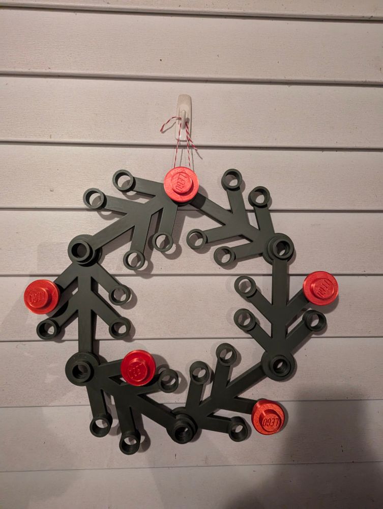 A life sized 3D printed Lego wreath with green branches and red berries.