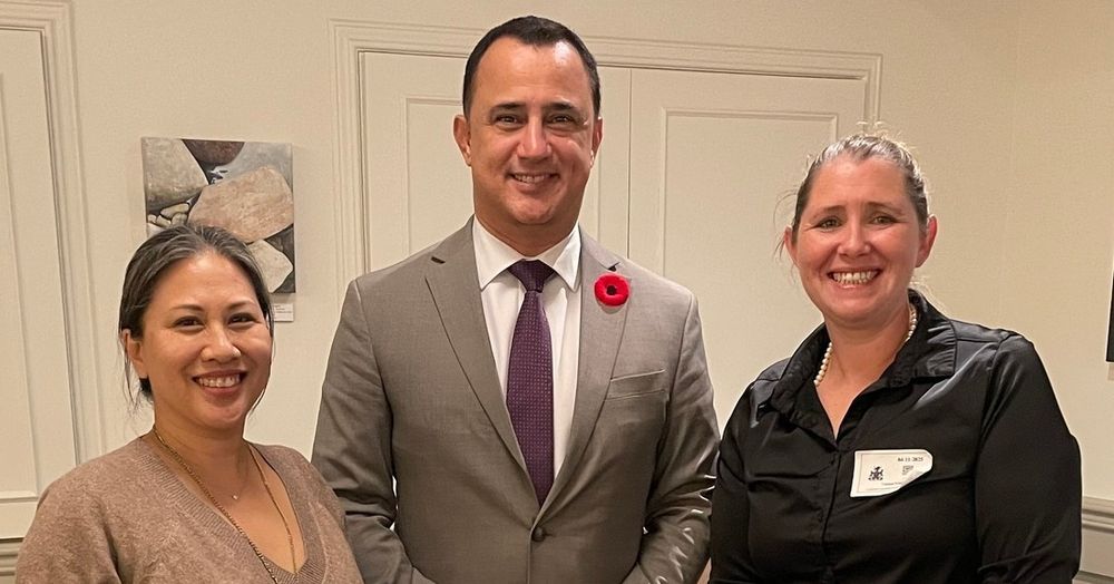 Three people stand smiling in a well-lit room. The man in the middle is Ontario Minister Michael Parsa. He wears a suit with a poppy pin.

He is flanked by two women , Myra Zettel and Sarah Klodnicki of Balance Support and Self Care Studios