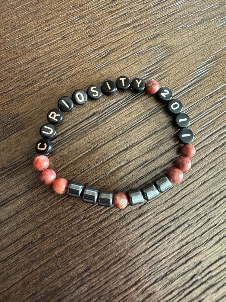 Friendship bracelet that says "Curiosity 2011" and also has six hematite beads representing rover wheels.