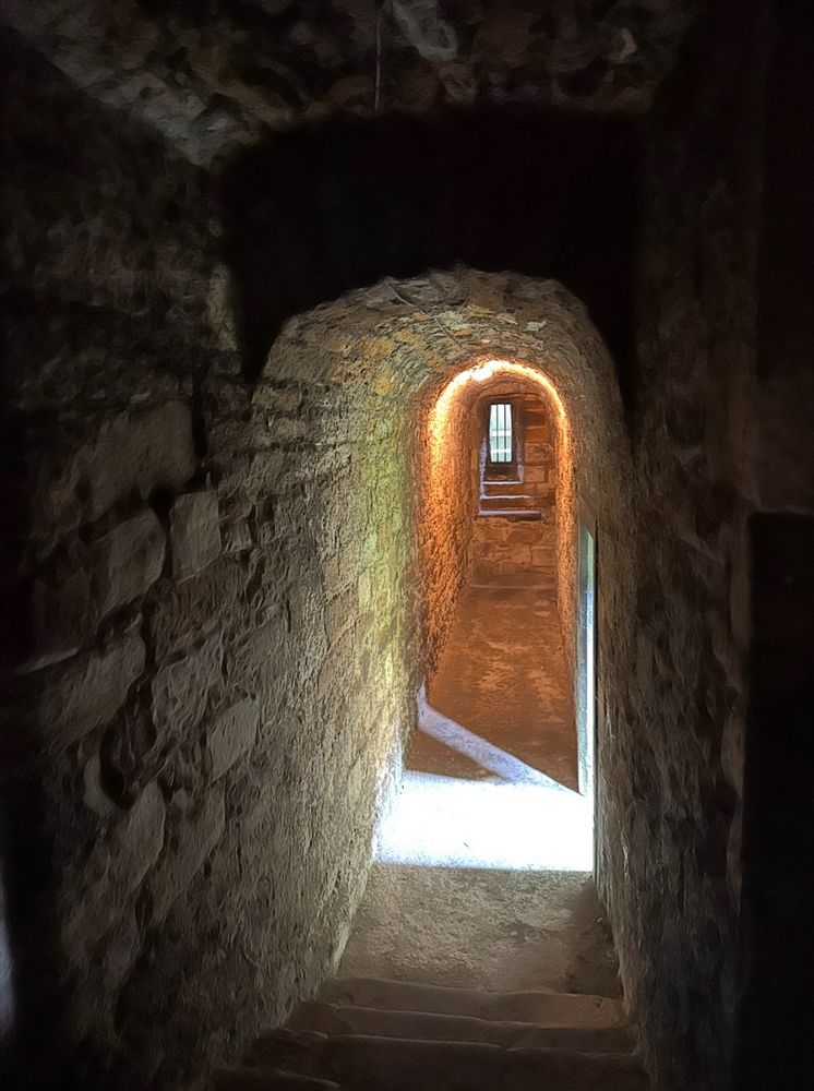 Photo is of a dead end path, in a mold-infested dungeon. One side of the tunnel leads to prison bars; the other side leads to darkness. But, in the middle of the path, a ray of light shines from an unseen doorway, illuminating the stone floor, and showing a possible escape route. Photography by Dawn Berkoski. 