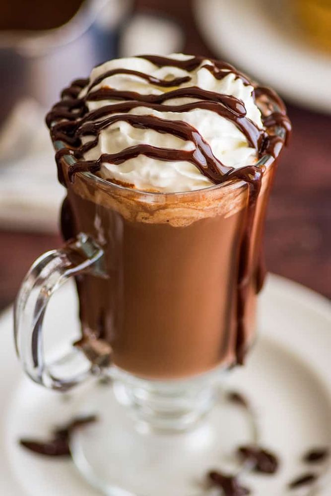 A glass of hot chocolate with whipped cream and chocolate syrup drizzled on top