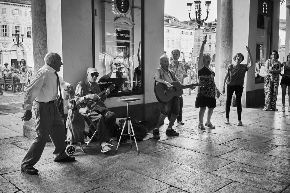 Five elderly men and women passionately sing and play the famous Neapolitan song under the porticoes of Piazza San Carlo in Turin, Italy. Black and white photograph by Paolo Benegiamo.