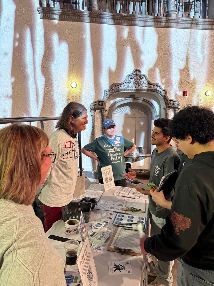 Three women standing behind a table labeled Indivisible Chicago, talking to two potential volunteers. 
