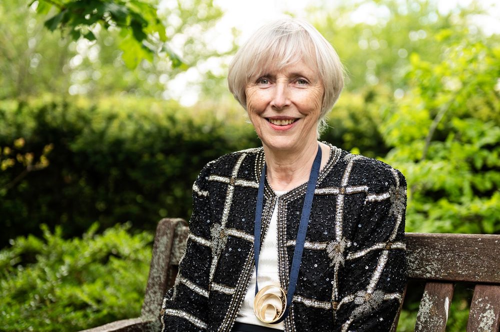 Caroline Dean sitting on a bench in front of some greenery.