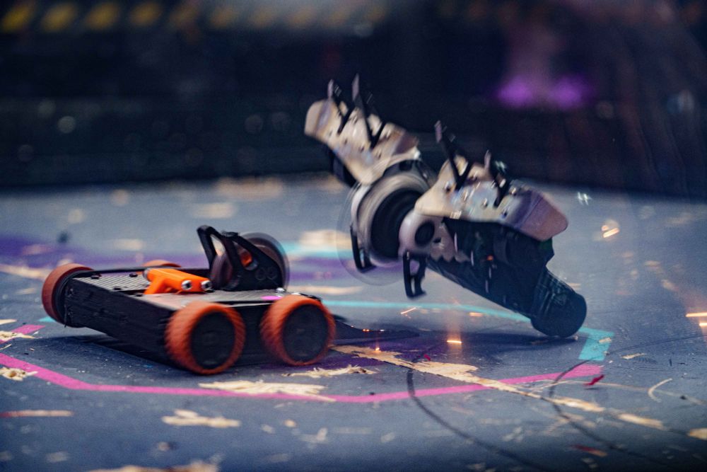 an image of two robots, Jackalope and Vapor Trail, fighting at the National Havoc Robot League. Jackalope, the orange and black robot, has flipped over Vapor Trail, the black and white robot. 