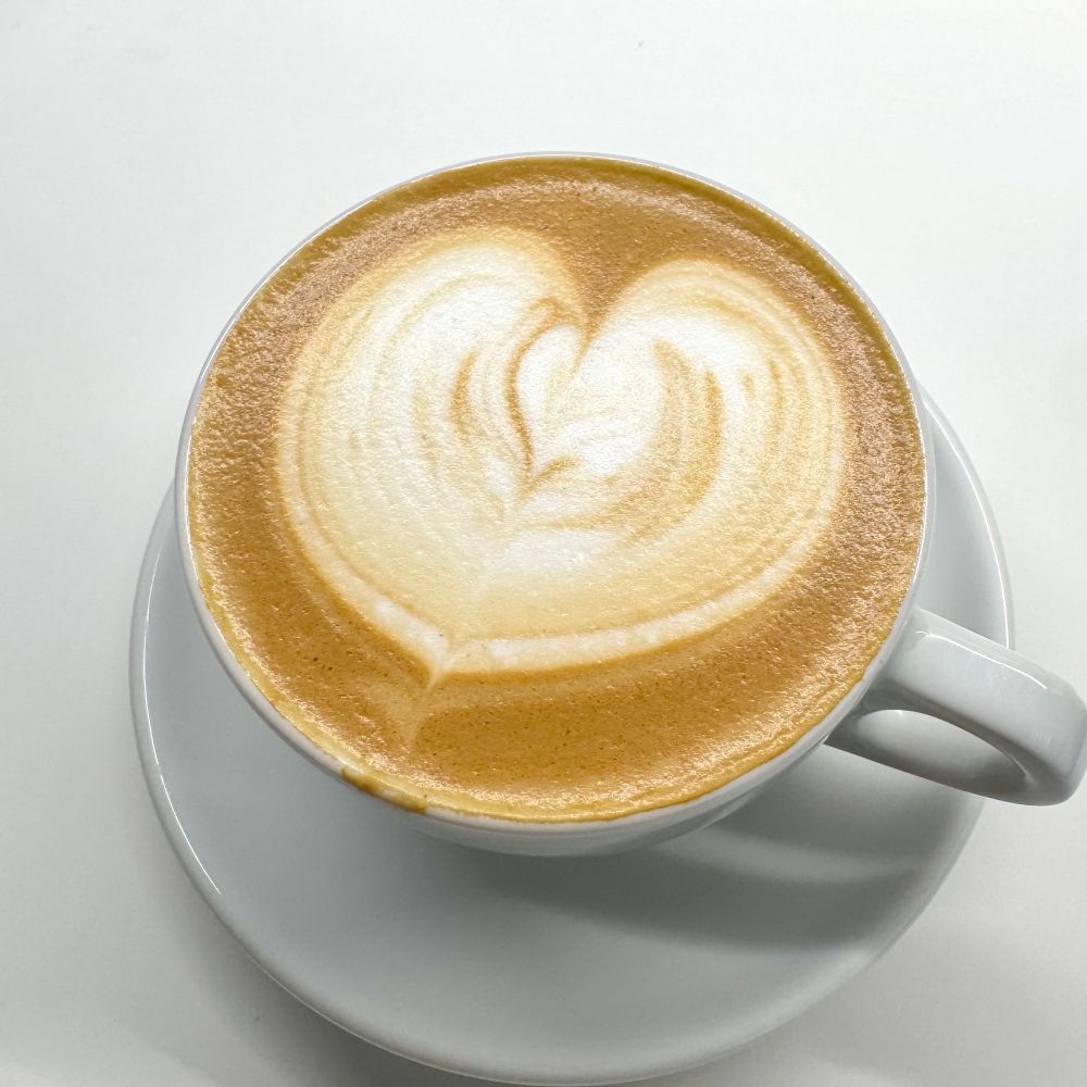 흰 도기잔에 든 커피와 좌우대칭이 맞지 않는 우유거품