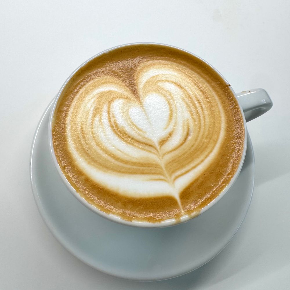 흰 도기잔에 든 커피와 결이 일그러진 우유거품. 대강 하트 모양이 보인다