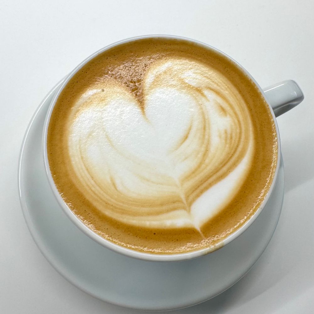 흰 도기잔에 담긴 커피와 우유거품. 모양은 하트지만 그 안의 결은 일그러져 무슨 모양인지 알아볼 수 없다. 비스듬히 내려다본 모습.