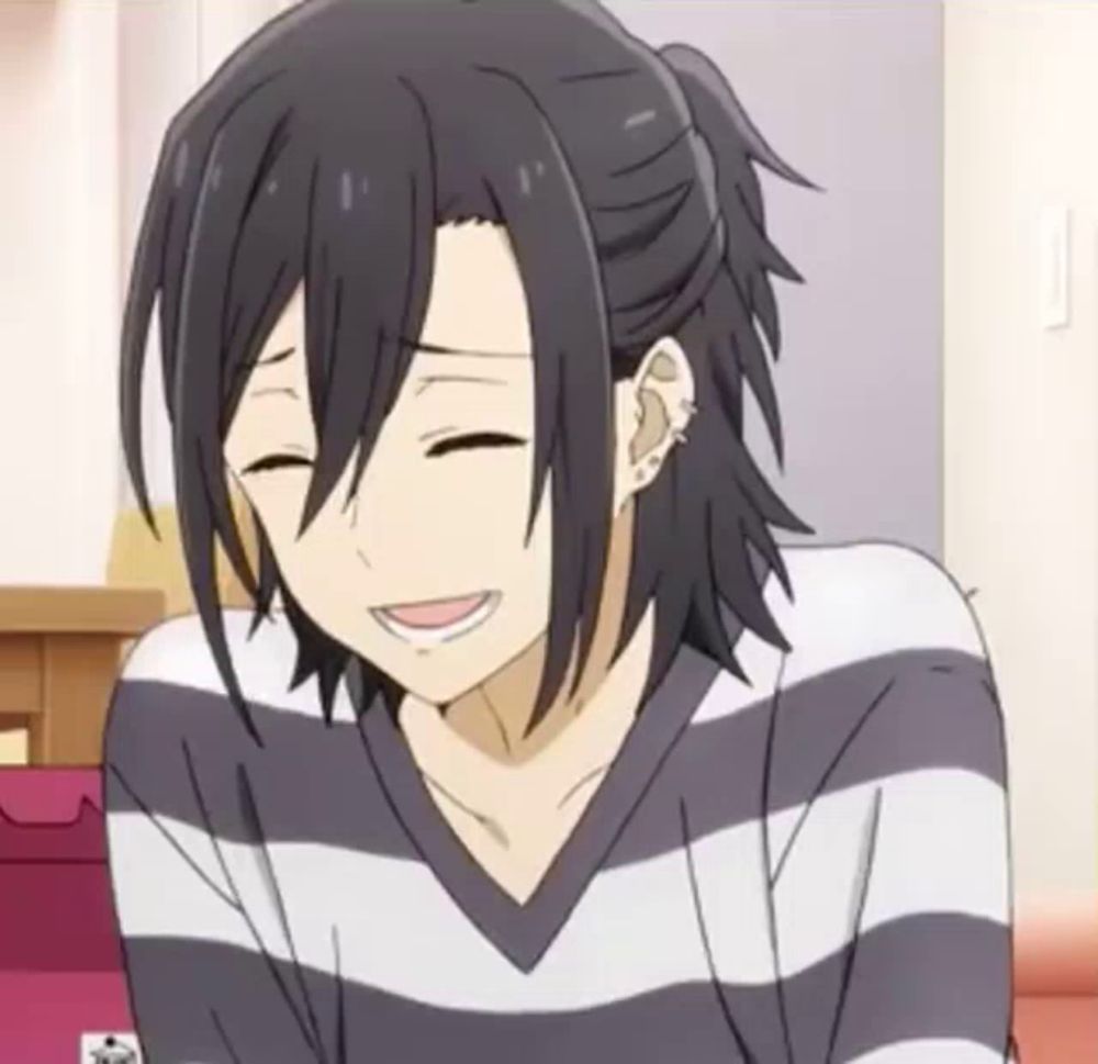 a man with long black hair is wearing a striped sweater and smiling