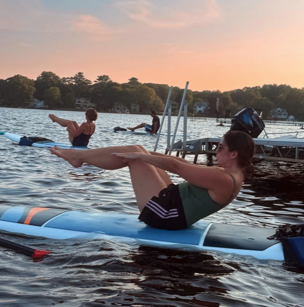 Elizabeth doing a really good variation of the Pilates 100 on a paddle board at sunset