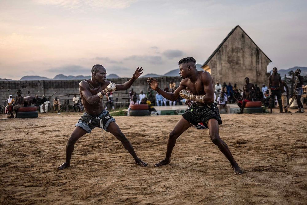 Dambe fighters engage in a bout during an amateur match in the Dei-Dei neighbourhood in Abuja. Dambe is a centuries-old combat sport rooted in the traditions of the Hausa people of Northern Nigeria. Traditionally practiced by the butcher class, known as Yan dambe, the sport features fighters with one hand wrapped in cloth and rope for striking, while the other remains free for defence. Kicks are allowed, and a match is won when an opponent touches the ground with any body part other than the feet. Once a highlight of harvest festivals and rural entertainment across the Sahel—including Chad and Niger—Dambe has evolved into an urban spectacle. Today, weekly matches in cities like Abuja draw large crowds, with organised leagues introducing formal rules, weight classes, and prize money. (Photo by OLYMPIA DE MAISMONT / AFP)