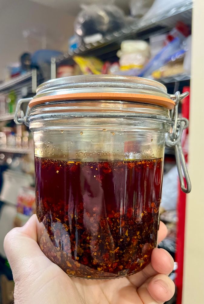 Hand holding a jar of freshly made Sichuan chili oil. 