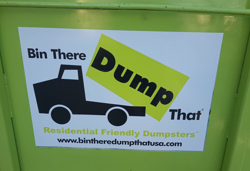 Green dumpster with a label on the side saying "Bin there, dump that"