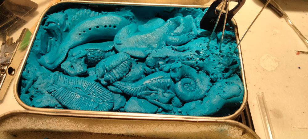 An Altoid Can containing a plethora of blue clay creatures all stacked up upon one another as they will be recycled into new clay creatures later.