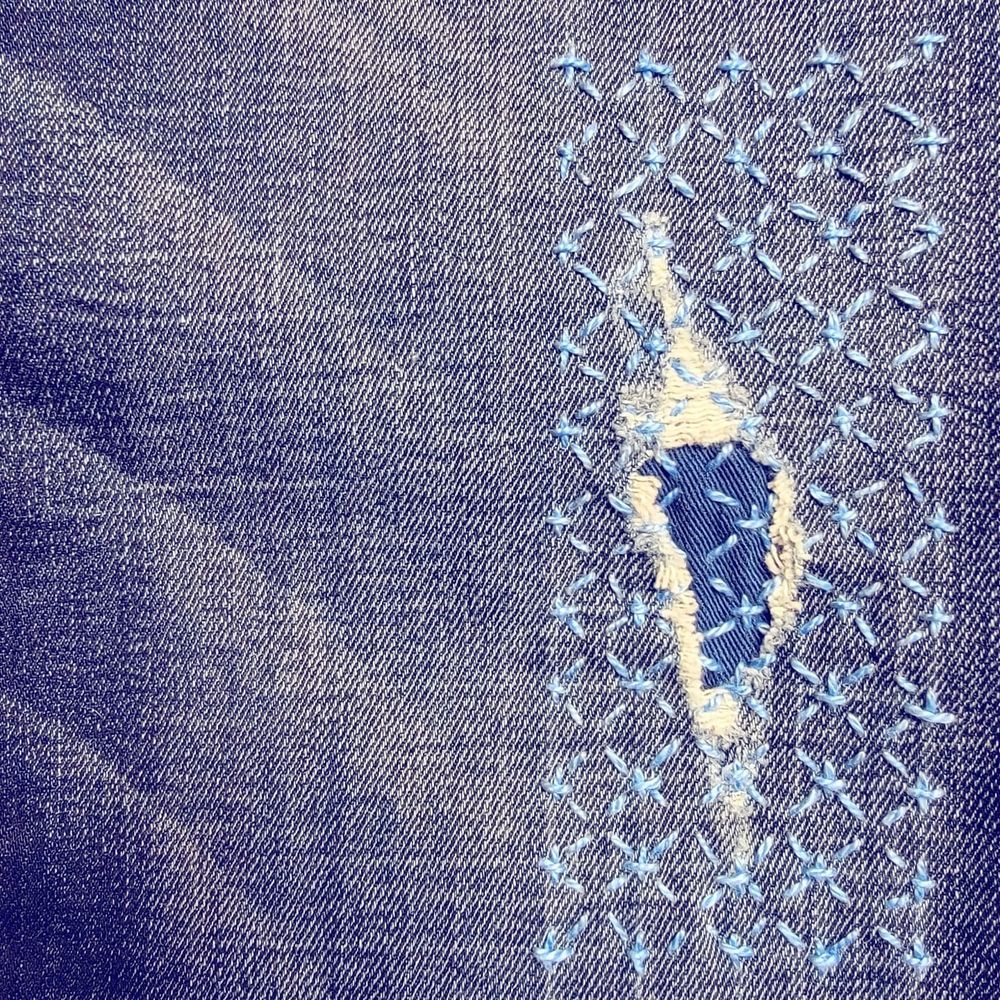 Photo of jeans mended with a reverse patch stitched by hand using sashiko stitches