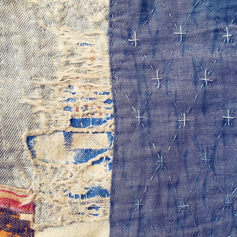 Photo of jeans mended with a reverse patch, and patches on top, stitched by hand using sashiko stitches