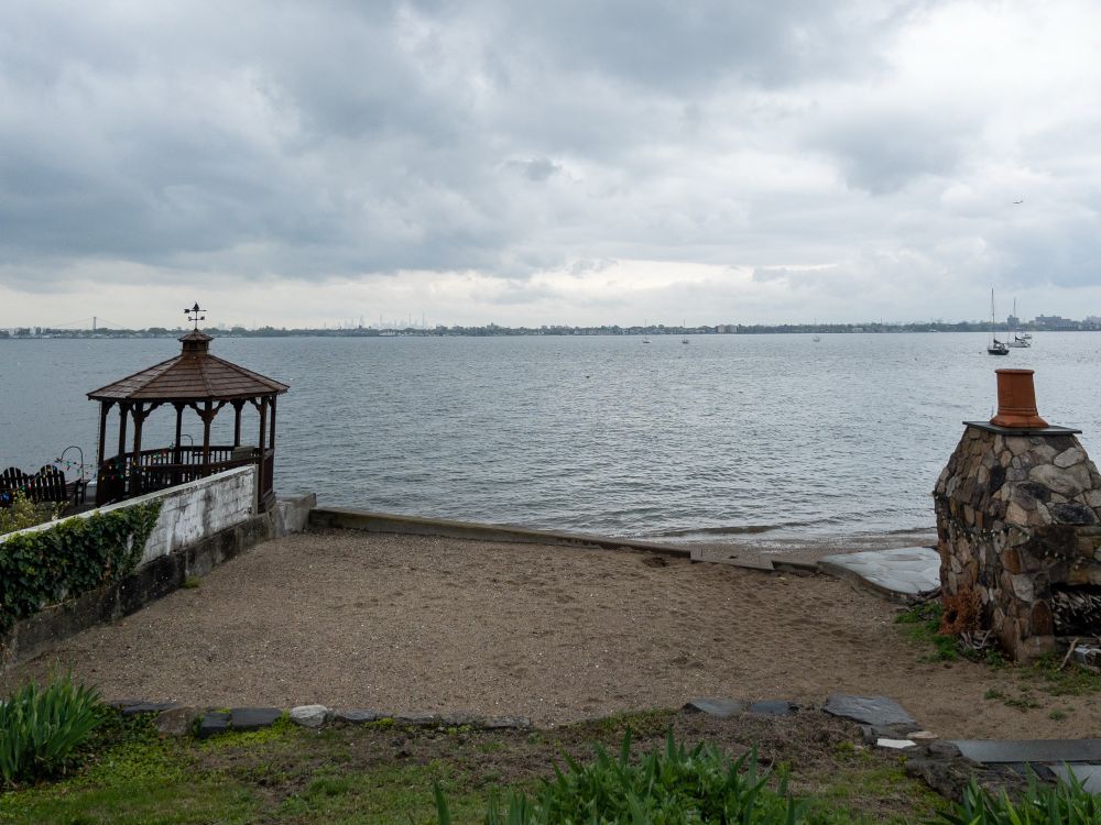 View southwest looking over a beach on City Island on a cloudy day with the Manhattan skyline faintly visible in the far distance.