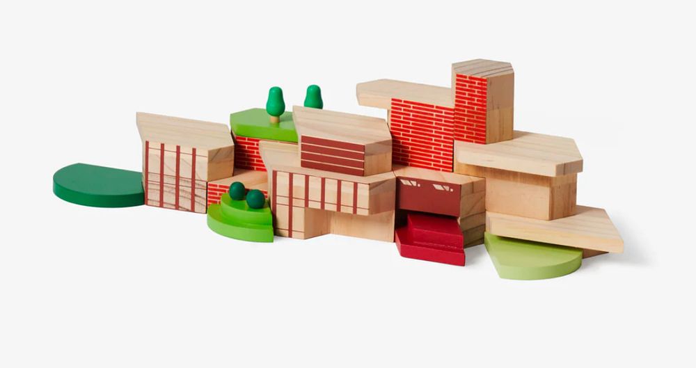 Wooden building blocks in the shape of Frank Lloyd Wright architectural design for a Usonian house: very angular and geometric, with red accents and panels. Trees and bushes added as well.