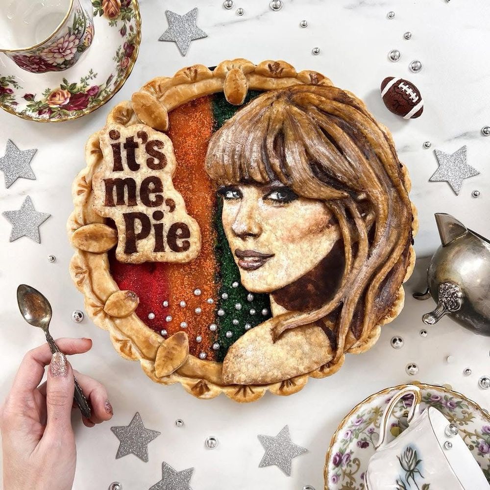 Decorative baked pie with a Taylor Swift’s face and the words "it's me, Pie" on top. Surrounded by teacups, a small football, and star decorations.