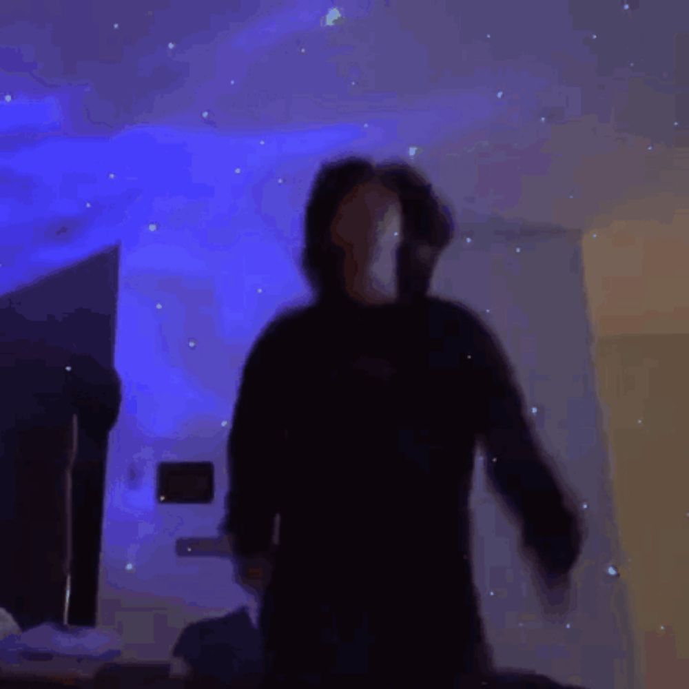 a person is dancing in a dark room with a galaxy projector on the wall .