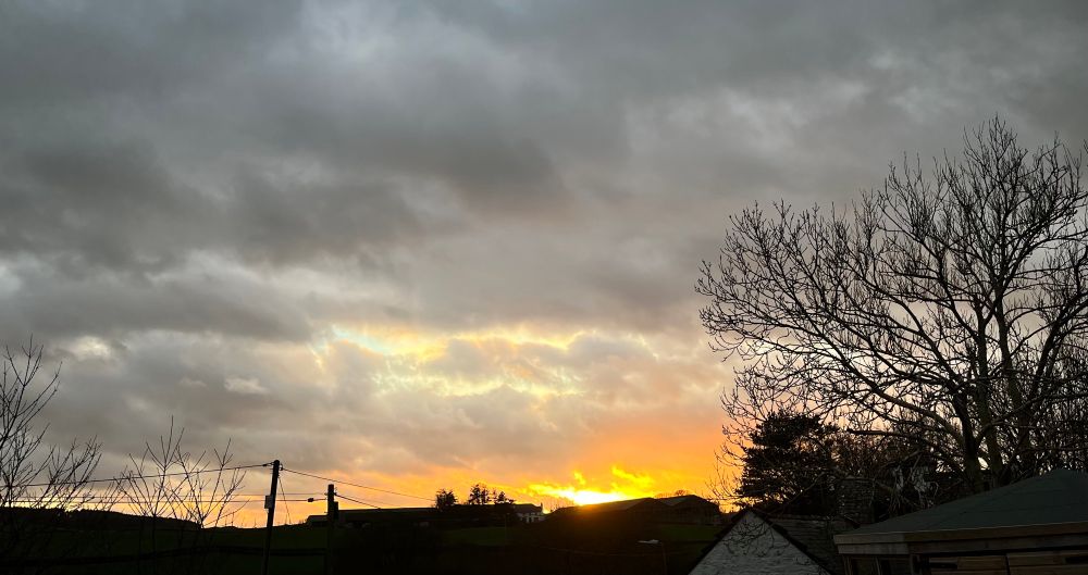 Sunset over a small hill. Houses and trees silhouetted against the sky.