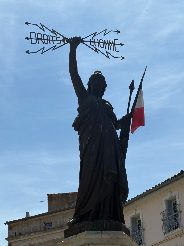 Une statue, représentant la république brandit dans sa main droite les Droits de l’Homme , symbolisé par des éclairs sous forme de flèches 