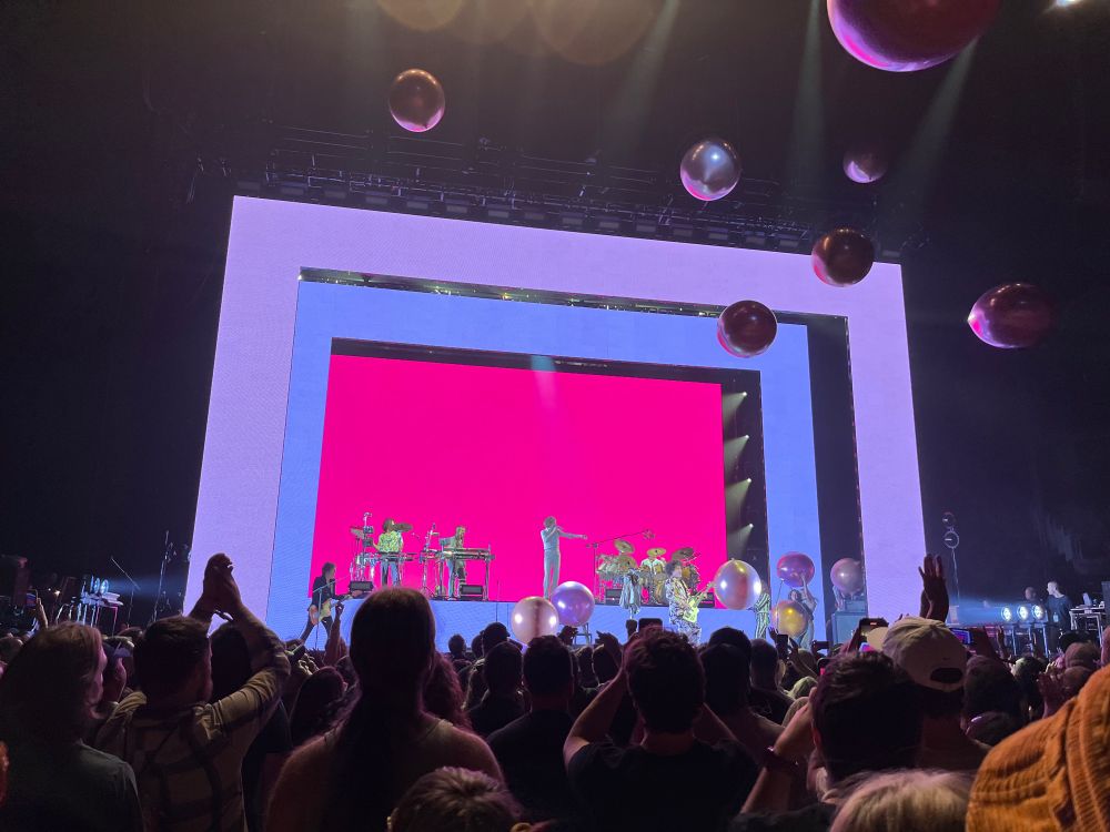 Beck performing on a neon set with balloons floating in the air.