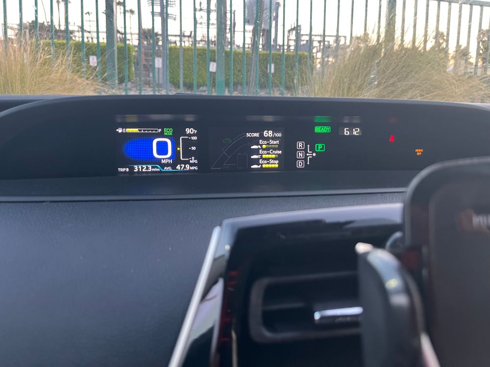 A Prius dashboard display showing the temperature as 90°F at 6:12AM. 