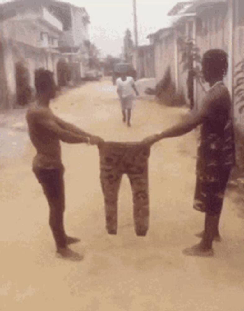 two men holding a pair of pants in their hands on a dirt road