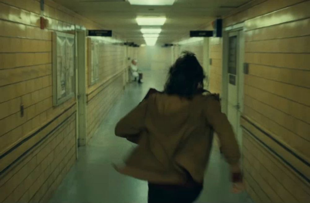 a person in a brown jacket is running down a hallway with a sign that says ' emergency room ' on it