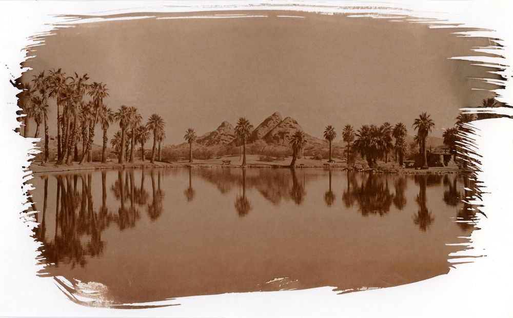 A salt type print of Papago Park. Originally shot on 8x10, this print was made using the 8x10 negative & a salt-typing kit from Lost Light Art. 

In the print, the red rocks famous in the park are seen beyond a fishing pond lined with palm trees. In the pond, reflections of the trees & rocks are seen. 