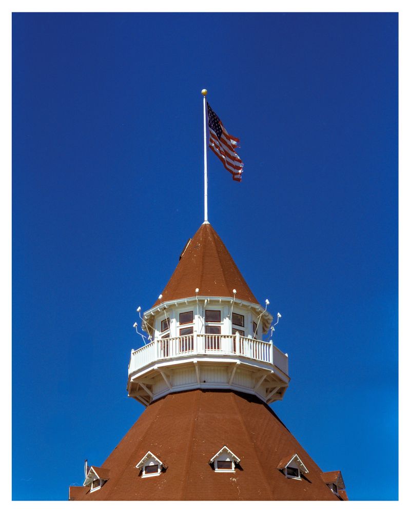A photograph of the top of the rotunda of the Hotel del Coronado. Brown shingles line the structure with a bright white walkway at the top of the rotunda. 