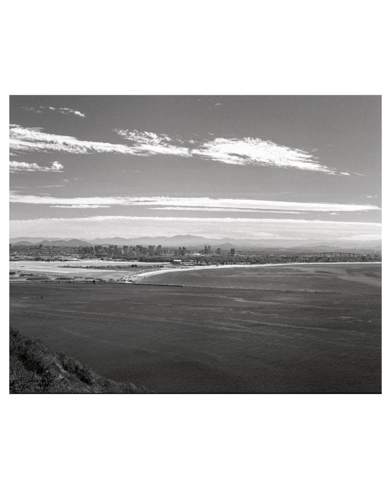 A black and white photograph of the city of San Diego, taken from Point Loma. In the photo, North Island, Coronado, and Downtown San Diego can all be seen. 