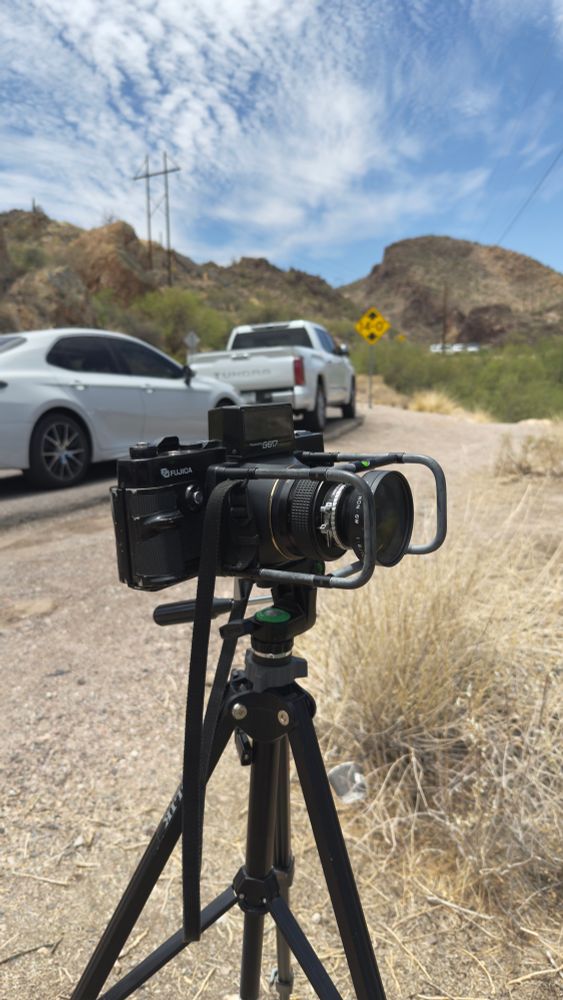 A photograph of the Fuji G617 on a tripod at Canyon Lake. In the background, cars are seen parked on the side of the road.