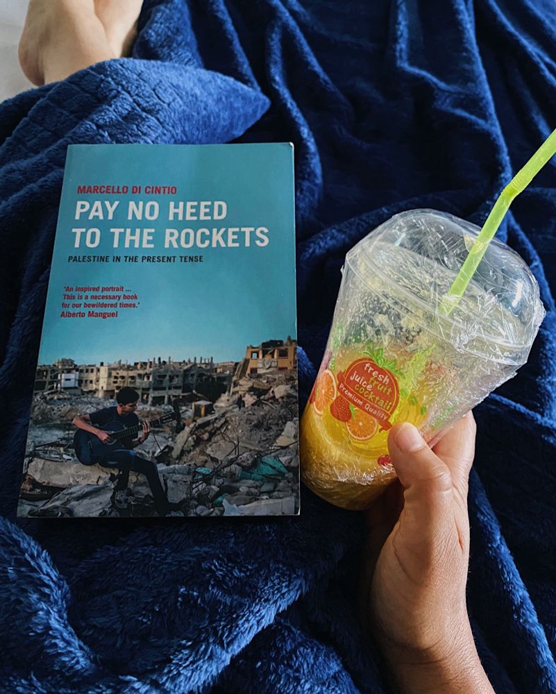 I’m in bed with a cold and have the book ‘Pay no Heed to the Rockets: Palestine in the Present Tense’ by Marcello di Cintio on my lap. A plastic cup full of lemon, ginger and honey juice is on my right hand. It has a bright green straw.