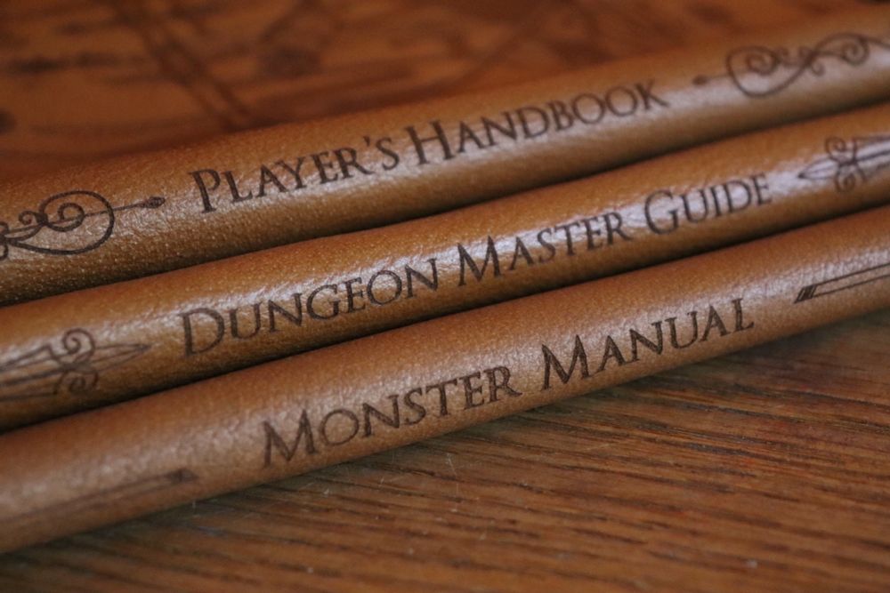 Three leather pieces that make up book sleeves, lying on top of each other, photographed at the fold/spine. They read 'Player's Handbook', 'Dungeon Master Guide' and 'Monster Manual'