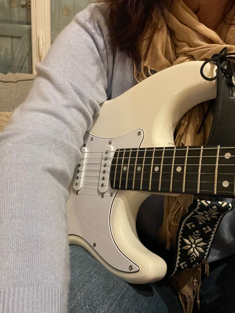 Buste de femme qui tient une guitare électrique blanche  on voit mon épaule et mon bras sur la guitare 