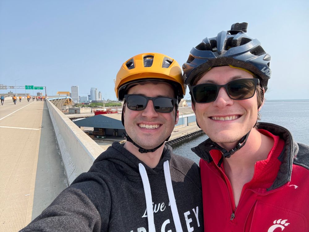 A selfie with the OP and the OP's partner with the bridge in the background and many cyclists riding on the road in the background
