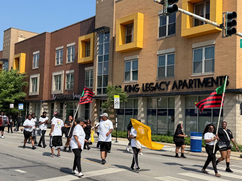 Participants walking in the parade with the Dr King Legacy Apartments in the background 