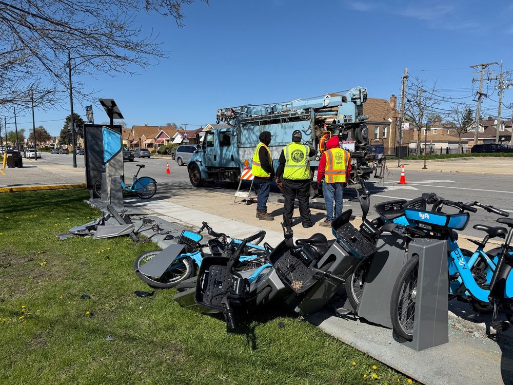 A divvy bike share rack smashed in many pieces with bikes lying on the ground, likely because a car crashed into it 
