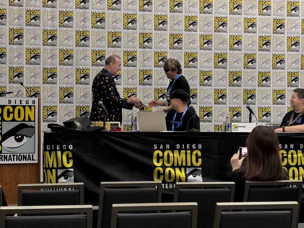 A man hands Kia Asamiya the INKPOt Award at SDCC while two men look on