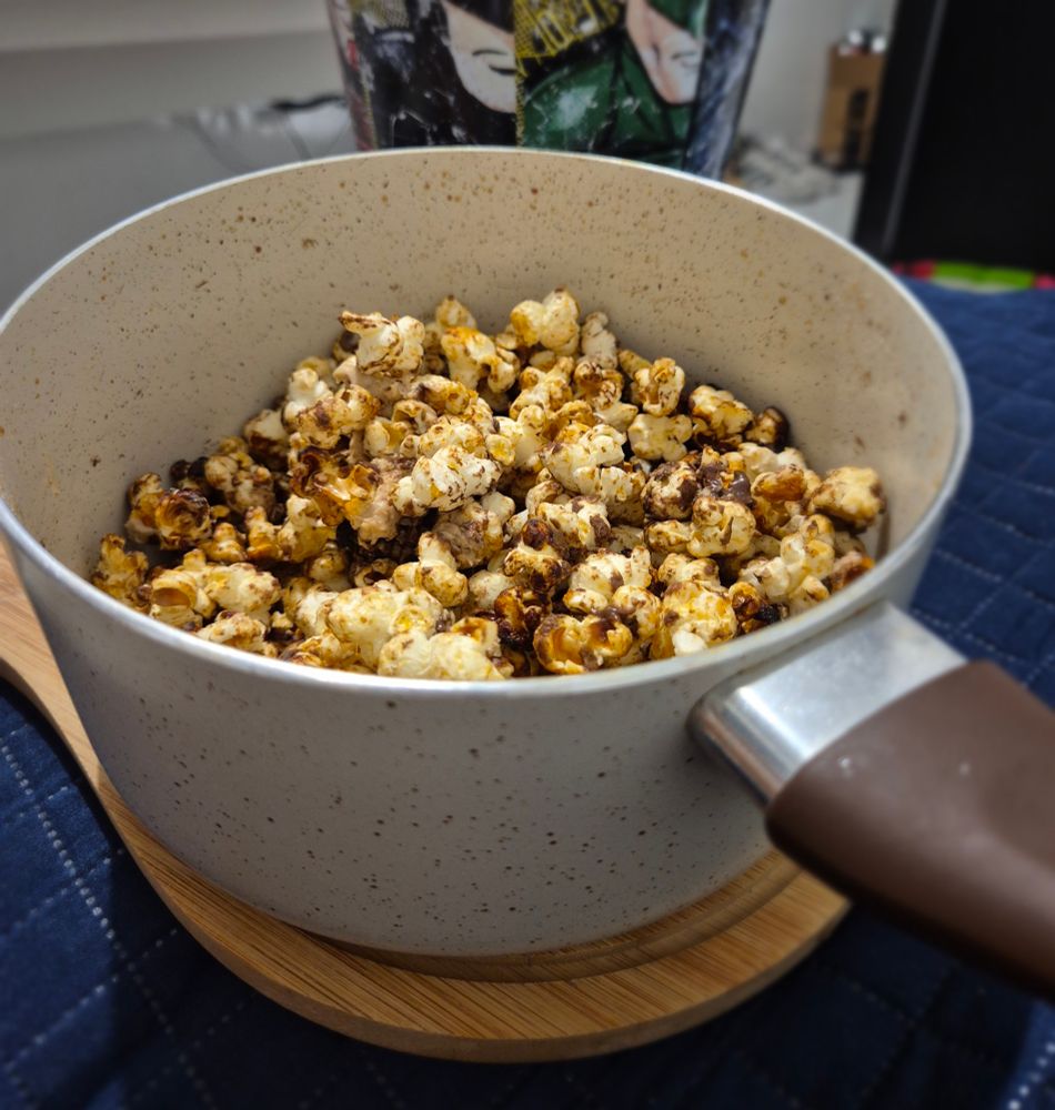 panela de pipoca doce feita, nesta ordem, com água fervente, açúcar, óleo, milho de pipoca e, depois, com sonho de valsa picotado espalhado na pipoca pronta 