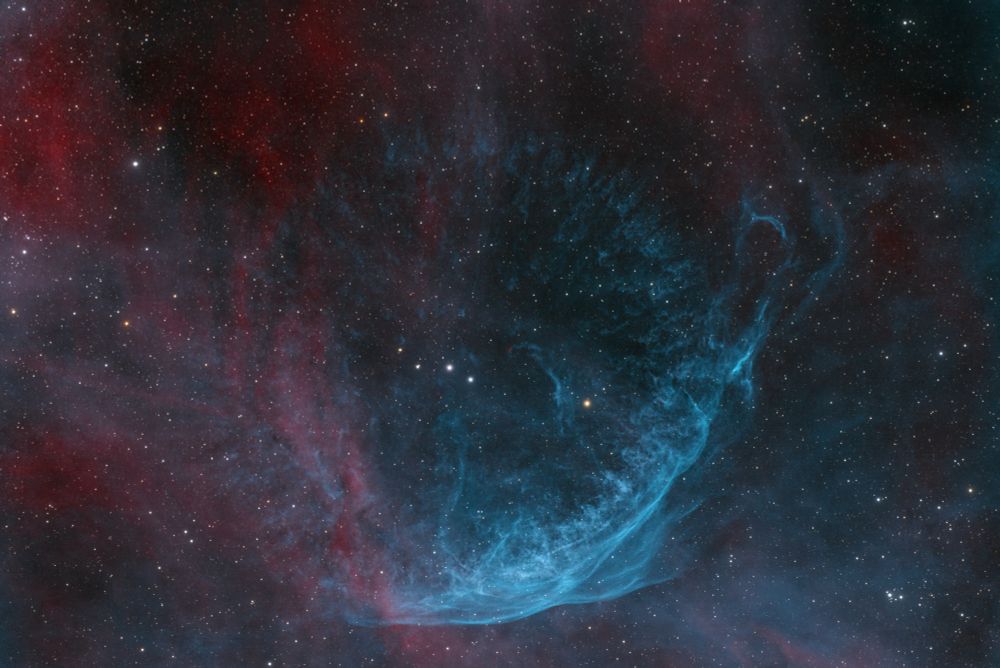 WR 134 is a dying Wolf-Rayet star about 6000 light years away from Earth in the constellation of Cygnus. The surrounding structure is formed by WR 134 blowing off massive amounts of its shell and its intense radiation. WR 134 is the second from right of the four lined up stars in the centre.