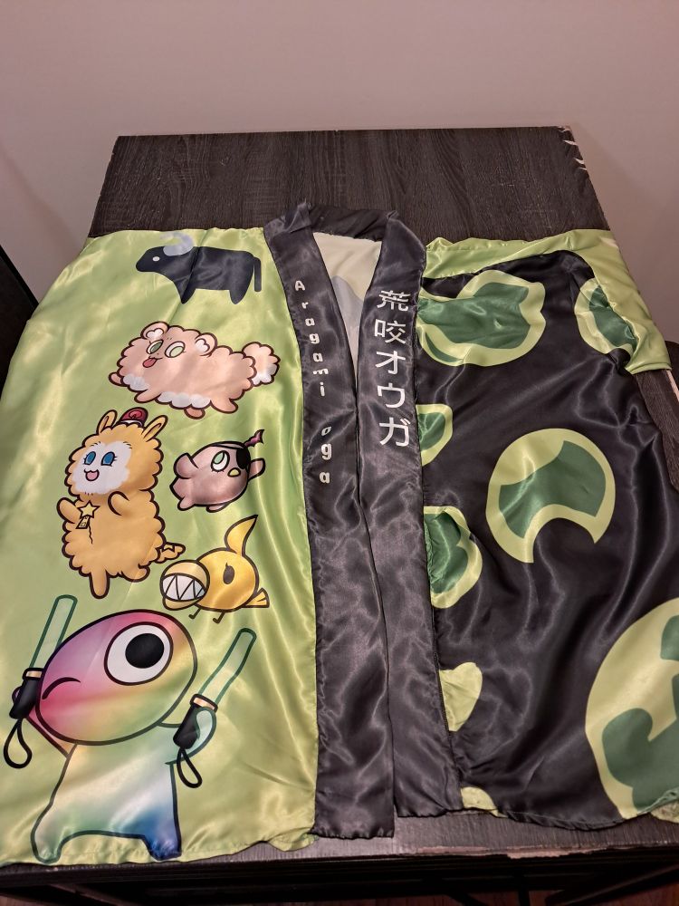 The front of the Aragami Oga Happi Coat. Oga's mascots are I n the left and a green and black pattern is on the right. 