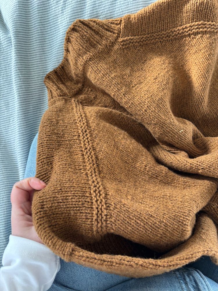 Brown knit sweater on blue duvet on bed.