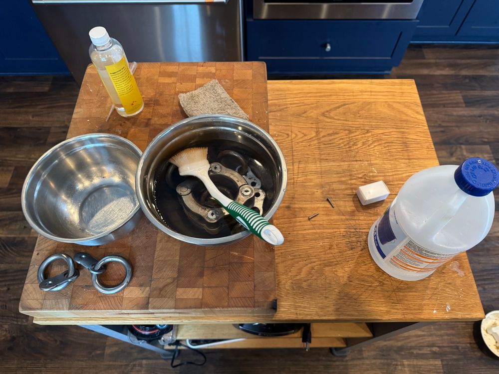 A small kitchen island with a couple of bowls, a bottle of vinegar, and a bottle of silicone oil. In one bowl is a set of heavy steel restraints soaking in vinegar
